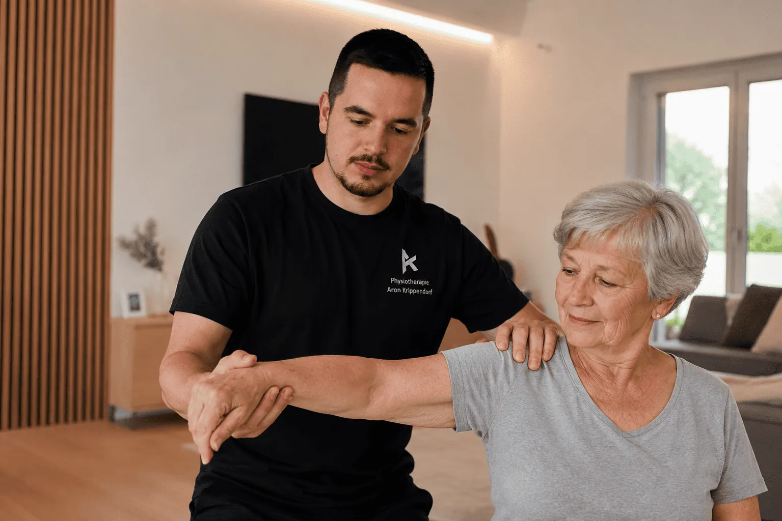 Therapeut mobilisiert die Schulter einer Seniorin im Wohnzimmer